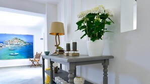 A modern living room with a grey console table, a blue stool, a white vase with flowers, and a painting of a coastal scene. - Kalidon Beach Hotel (Samos)