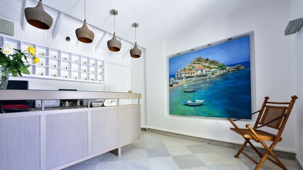 A modern kitchen with a white cabinet, a wooden chair, and a painting of a coastal scene on the wall. - Kalidon Beach Hotel (Samos)