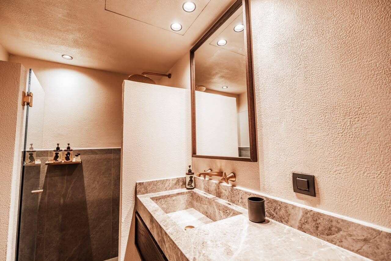 Un baño con lavamanos de mármol, un espejo grande y zona de ducha.