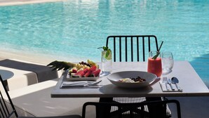 A poolside table with a meal, a drink, and a view of a pool and mountains. - Doryssa Seaside Resort (Samos)
