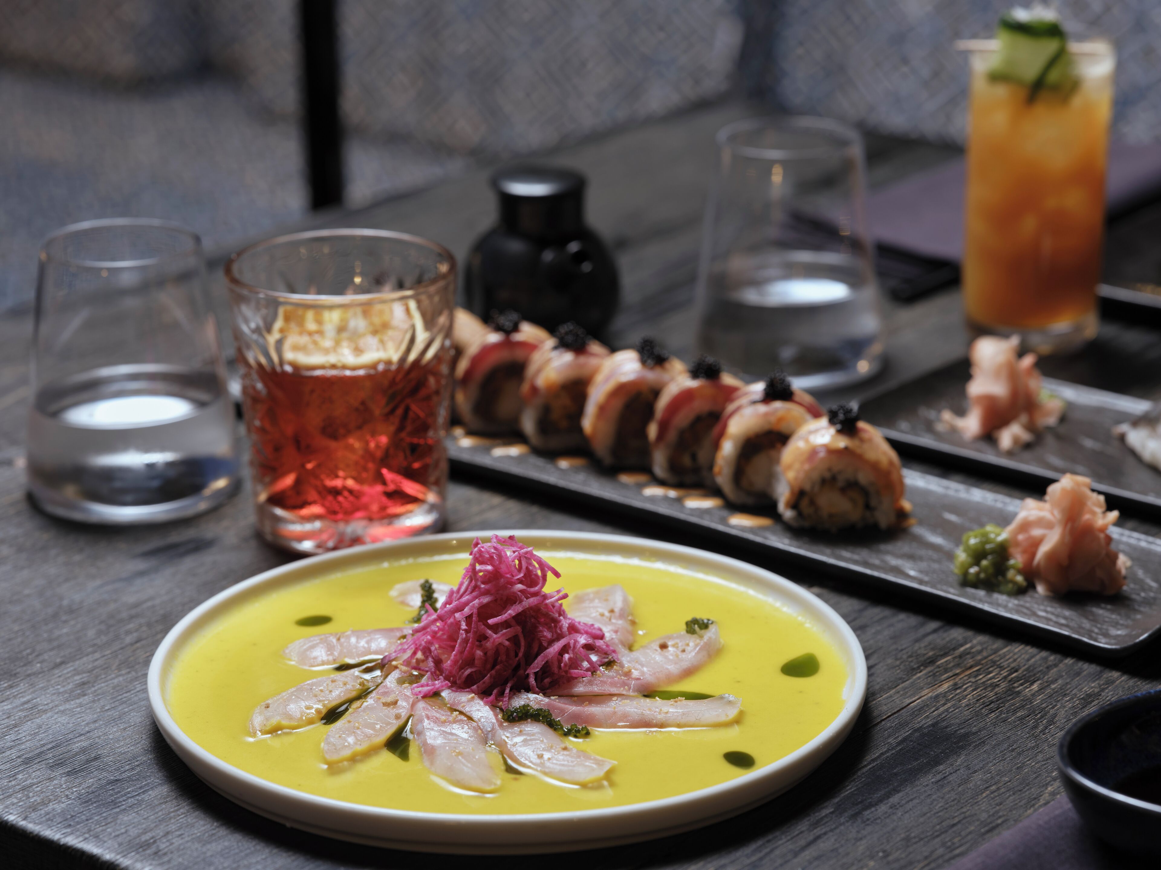 A dining table with a variety of dishes, including sushi, a bowl of soup, and a glass of tea.