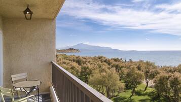 A balcony with a table and chairs, overlooking a coastal landscape with trees and a distant mountain.