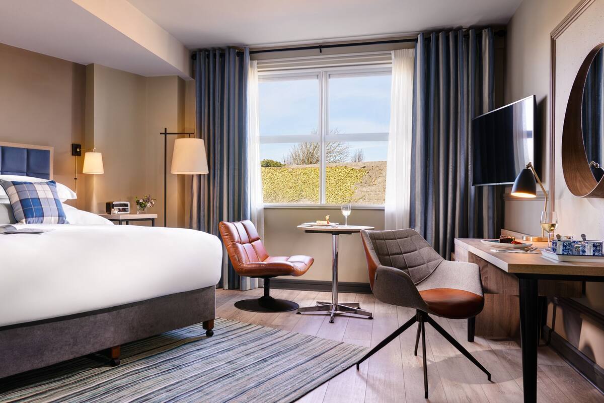 A hotel room with a large bed, a desk with a chair, a TV, and a window with curtains.