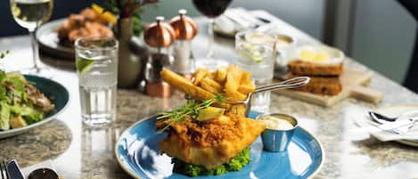 A dining table with a plate of fish and chips, a glass of white wine, and a glass of red wine.