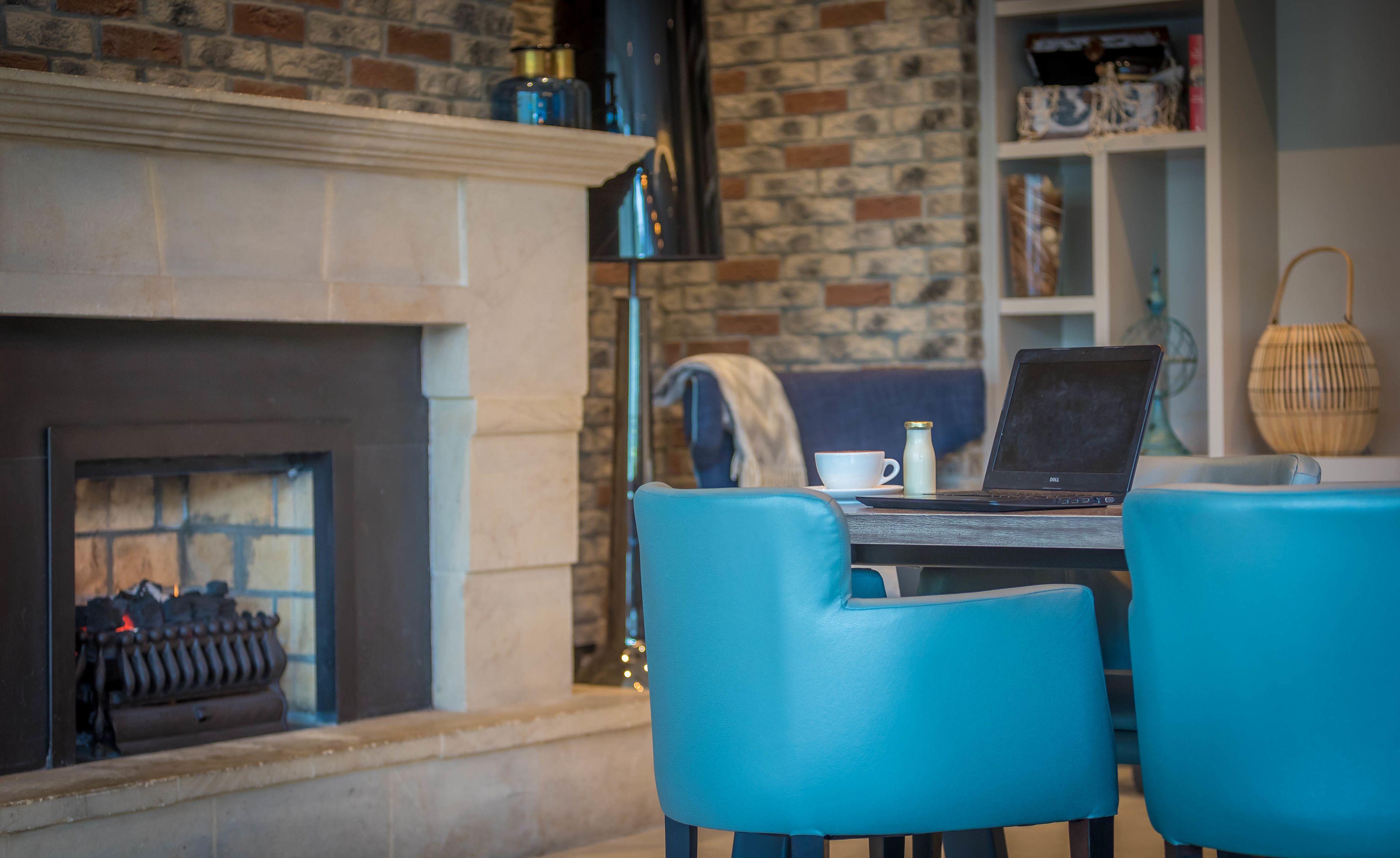 Una habitación acogedora con chimenea, una laptop sobre una mesa y sillas azules.