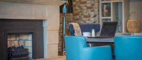 Una habitación acogedora con chimenea, una laptop sobre una mesa y sillas azules.