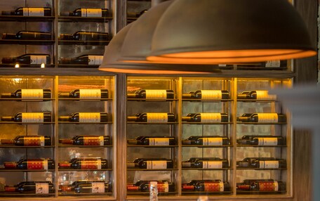 A wine cellar with shelves of wine bottles, a dining table set with glasses and cutlery, and a hanging light fixture.