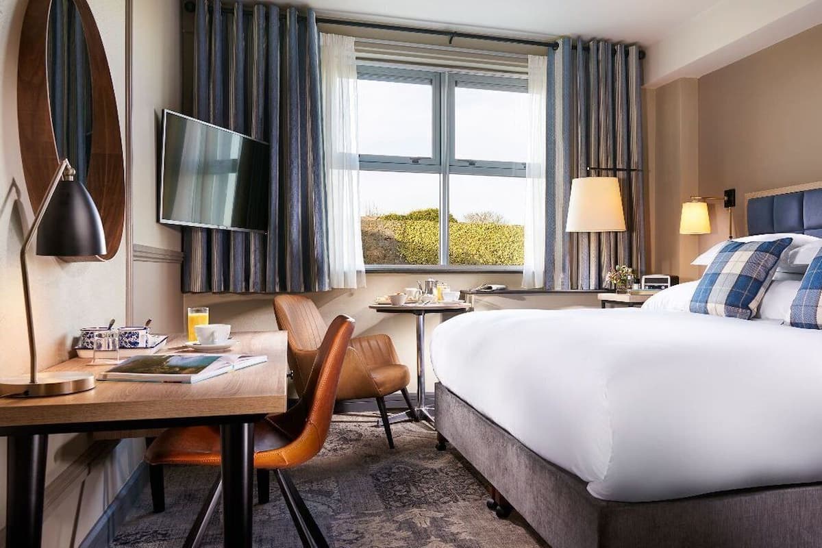 A hotel room with a large bed, a desk with a chair, a TV, and a window with curtains.