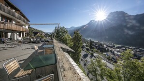 A terrace with outdoor seating, overlooking a town and mountains. - Engadiner Boutique-Hotel GuardaVal (Scuol)