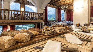 A bakery display with various breads and pastries, wooden tables, and a balcony overlooking mountains. - Engadiner Boutique-Hotel GuardaVal (Scuol)