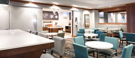 Un hall de hotel con una recepción, zonas de estar y una estación de café.