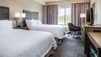 A hotel room with two beds, a desk, a chair, a TV, and a window with curtains.
