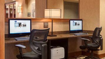 A hotel workspace with two Lenovo computers, two black office chairs, a printer, and a lamp.