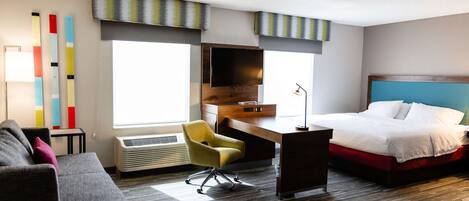 A hotel room with a bed, a desk, a chair, a TV, and a sofa.