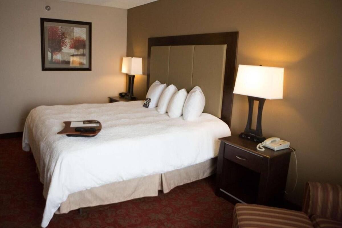 A hotel room with a large bed, two bedside lamps, a desk with a telephone, and a chair.