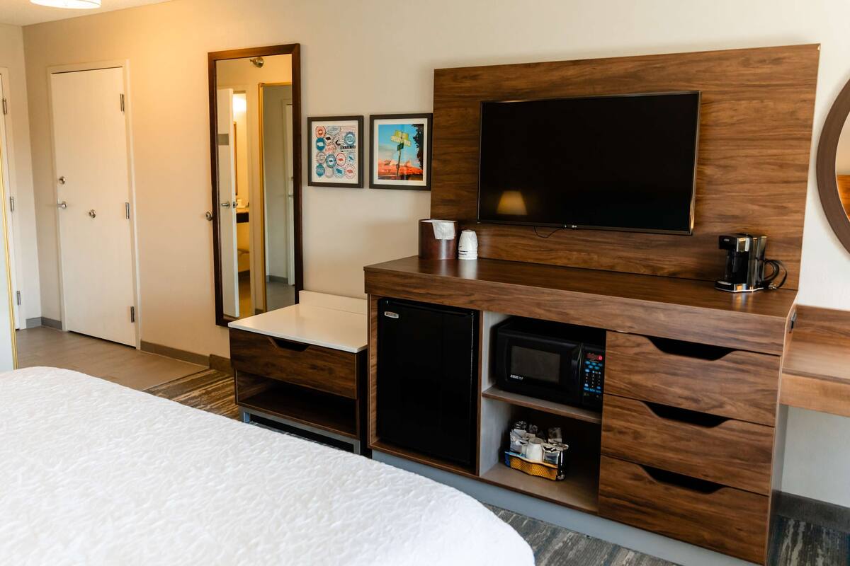 A hotel room with a bed, a wooden dresser with a television, a microwave, and a coffee maker.