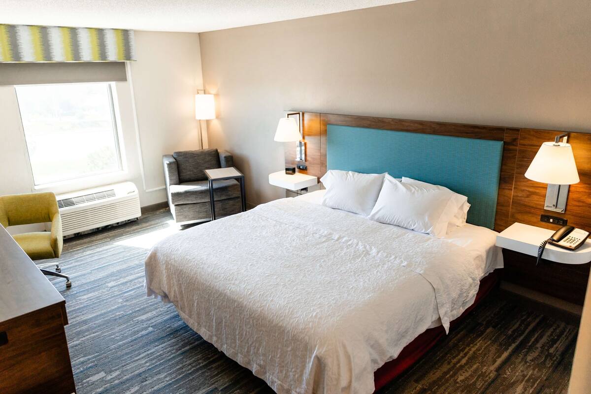 A hotel room with a large bed, bedside tables, a desk, a chair, and a window.