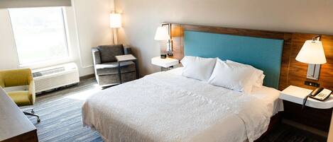 A hotel room with a large bed, bedside tables, a desk, a chair, and a window.
