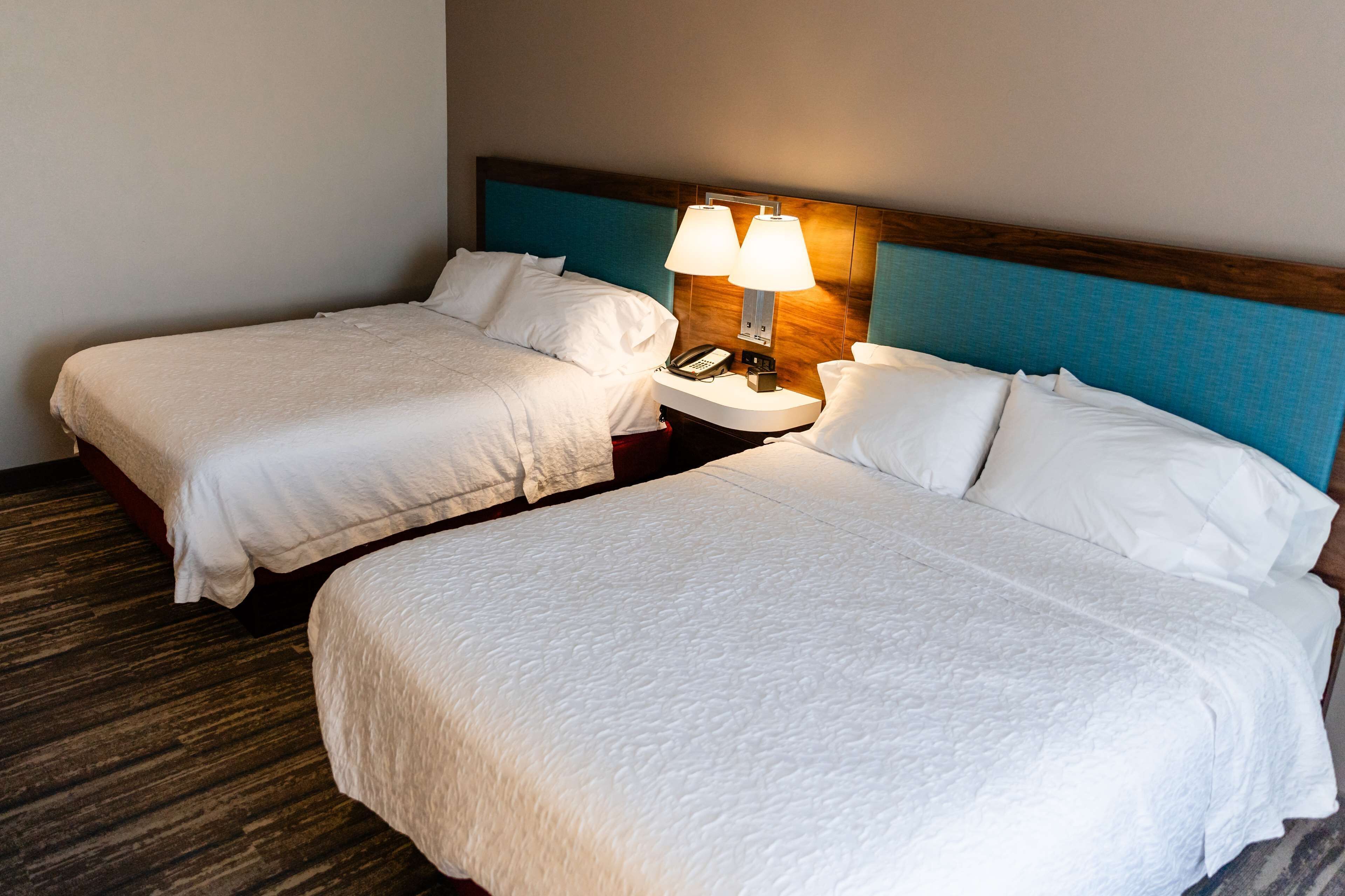 Two single beds with white linens, a wooden headboard, a bedside table with a lamp, and a phone.