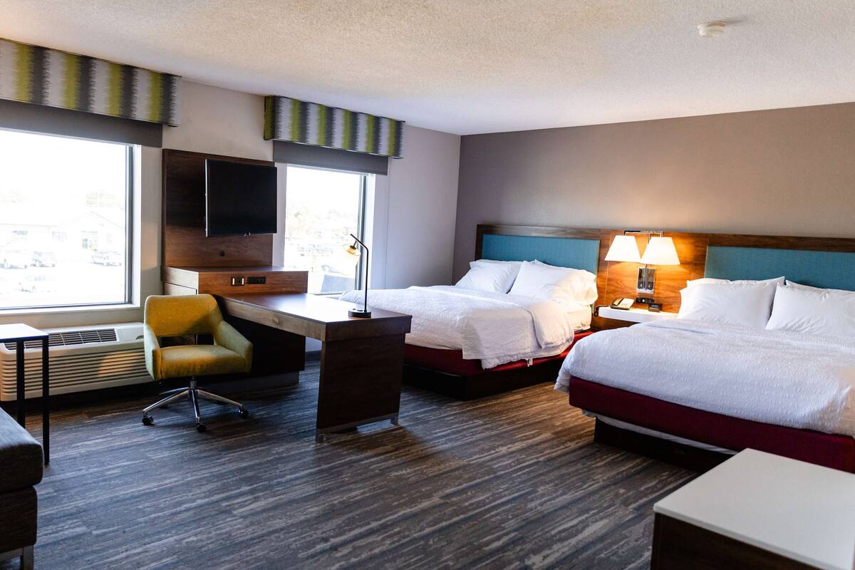 A hotel room with two beds, a desk, a chair, and a TV.