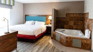 A hotel room with a large bed, a separate bathroom with a bathtub, and a desk with a lamp.