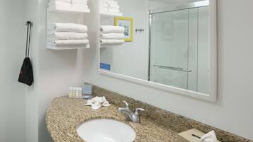 A bathroom with a granite countertop sink, a large mirror, and a glass shower door.