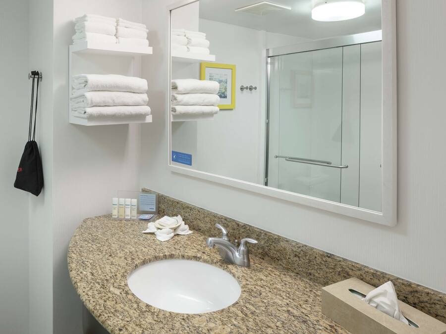 A bathroom with a granite countertop sink, a large mirror, and a glass shower door.