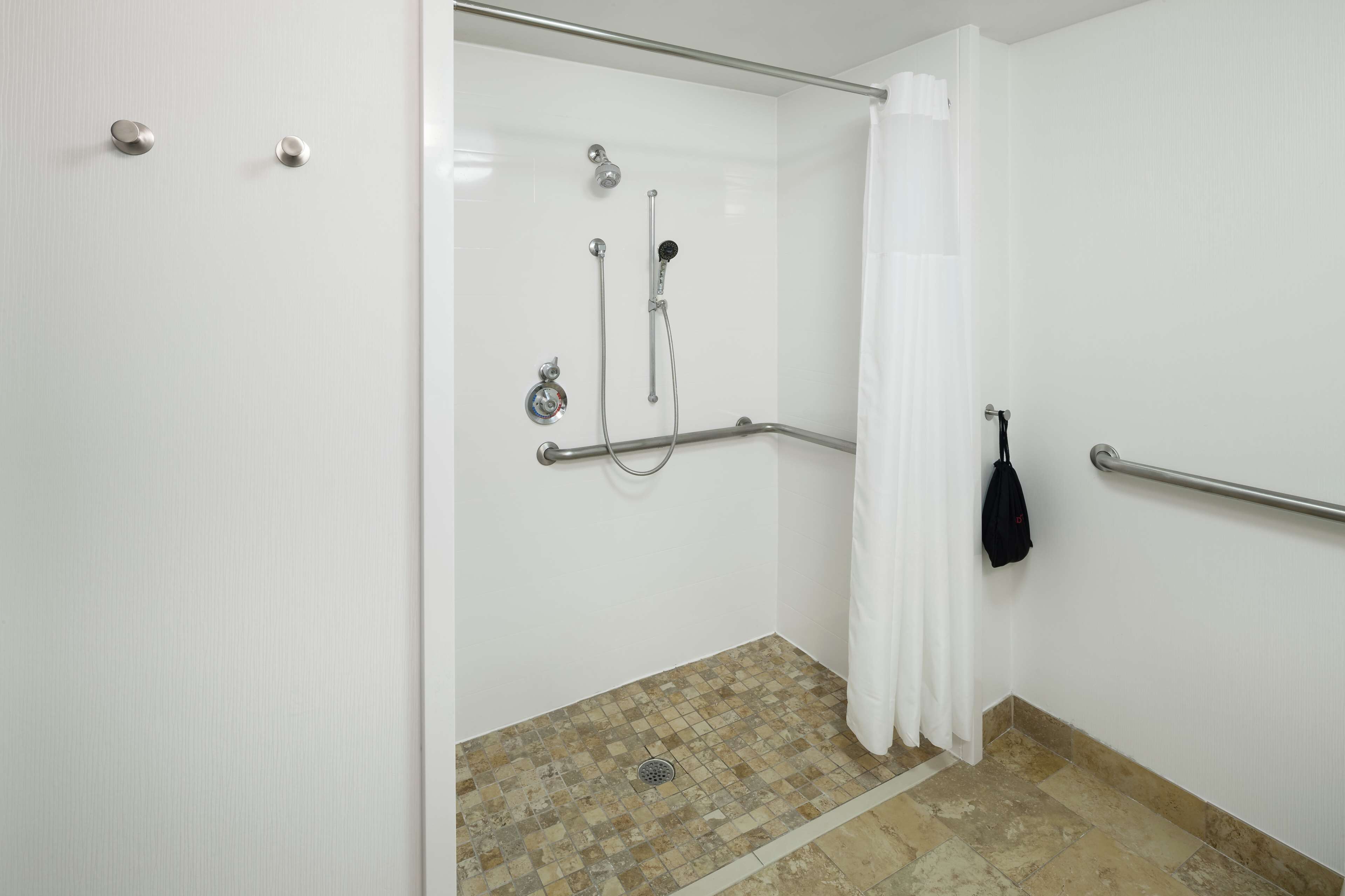 A shower area with a glass door, a grab bar, a showerhead, and a drain.