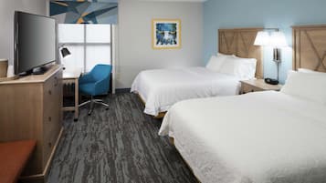 A hotel room with two beds, a desk with a TV, a chair, and a lamp.