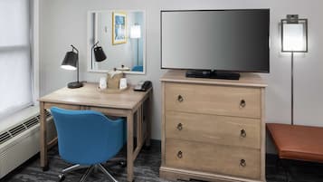 Une chambre d’hôtel équipée d’un bureau, d’une chaise, d’une télévision, d’une commode et d’un banc.