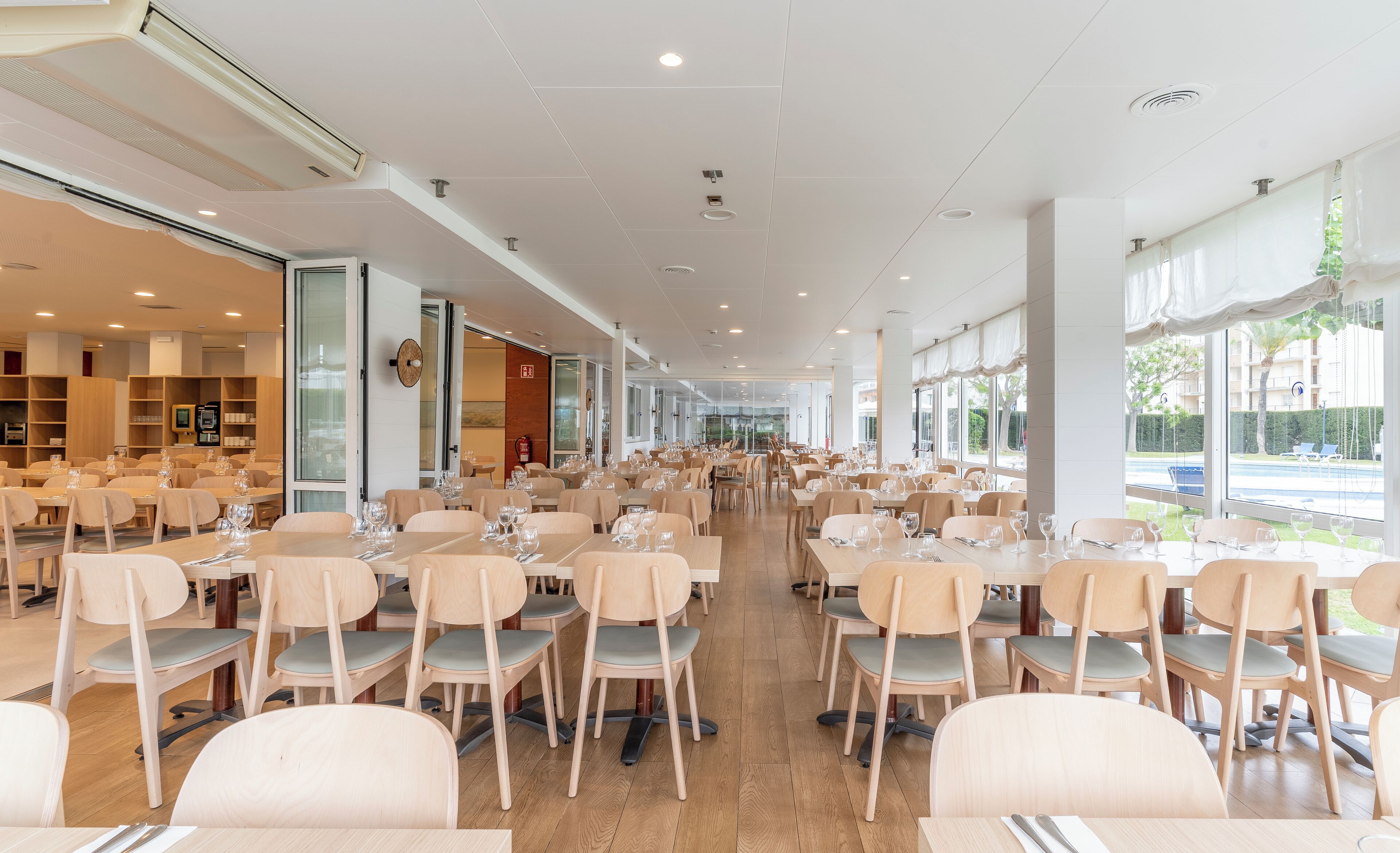 Un comedor espacioso con varias mesas y sillas, amplias ventanas que ofrecen vistas al exterior y un diseño moderno del techo.