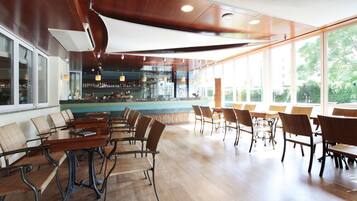 A spacious indoor area with wooden flooring, multiple seating arrangements, and large windows providing natural light.
