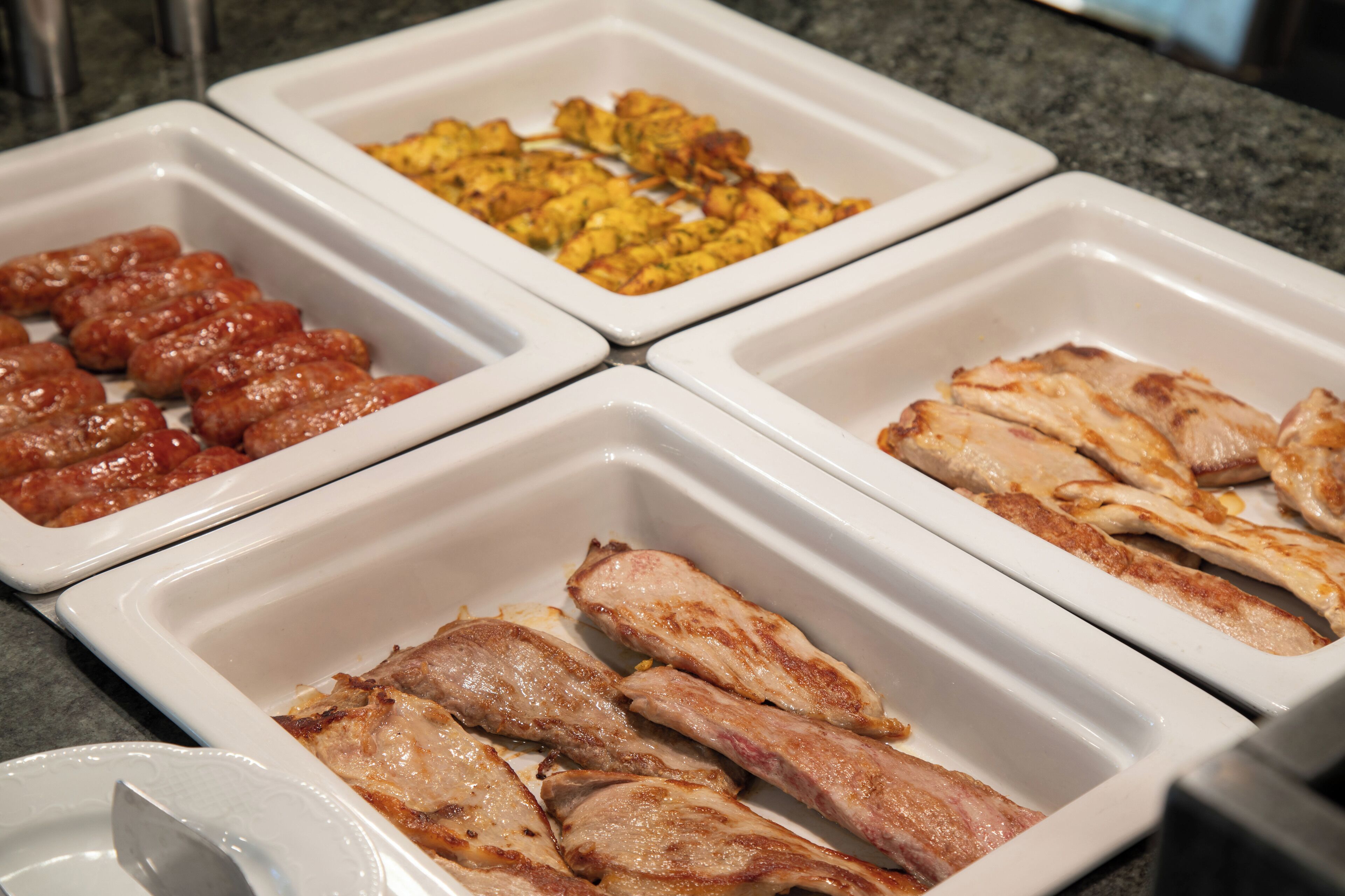 Un buffet proposant une variété de plats, notamment des saucisses, du poulet frit et un plat de légumes.