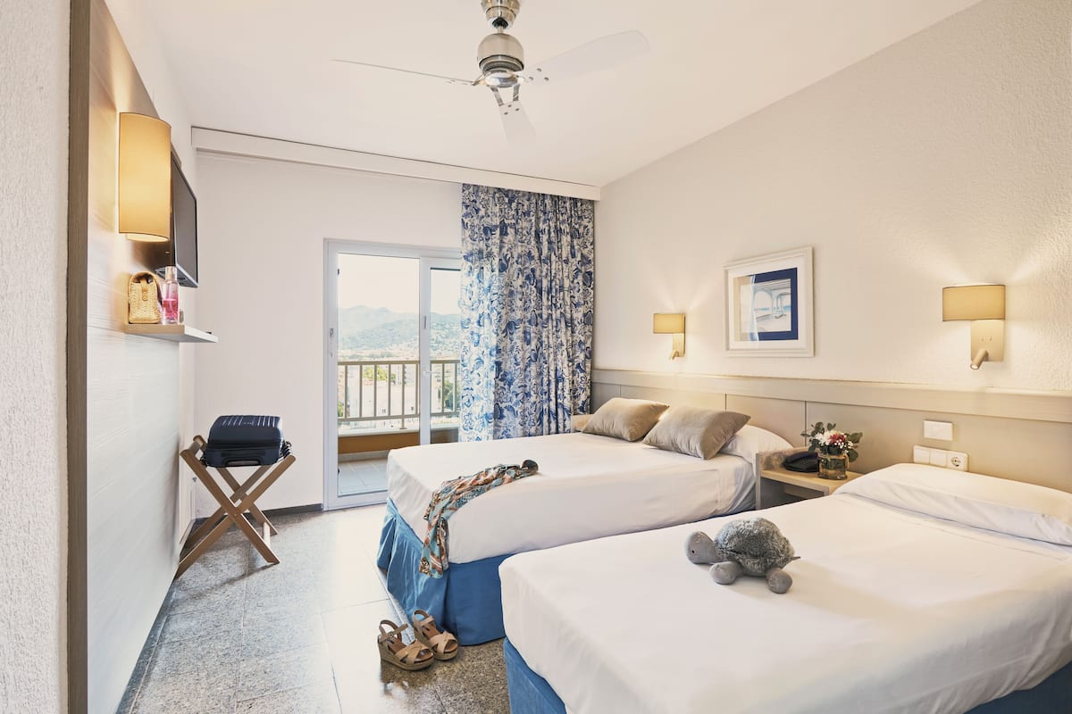 A hotel room with two beds, a ceiling fan, a TV, and a balcony with a view.