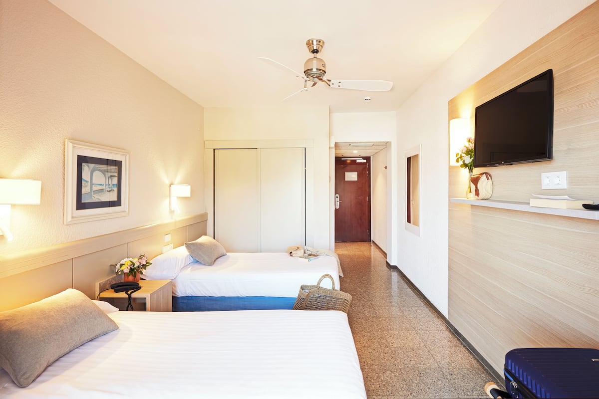 A hotel room with two beds, a ceiling fan, a TV, and a desk with a lamp and phone.