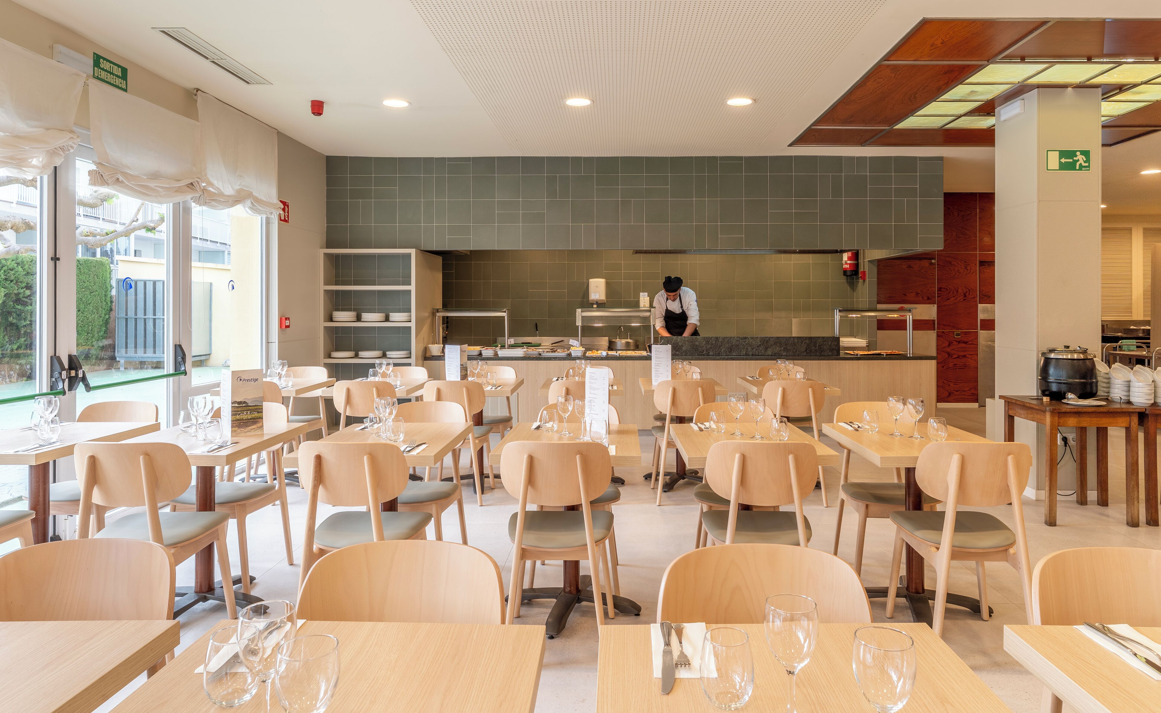 Un ristorante con diversi tavoli e sedie, una zona cucina e vista all'esterno.