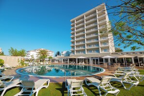 A pool area with lounge chairs, a swimming pool, and a multi-story building with balconies. - Prestige Goya Park (Roses)