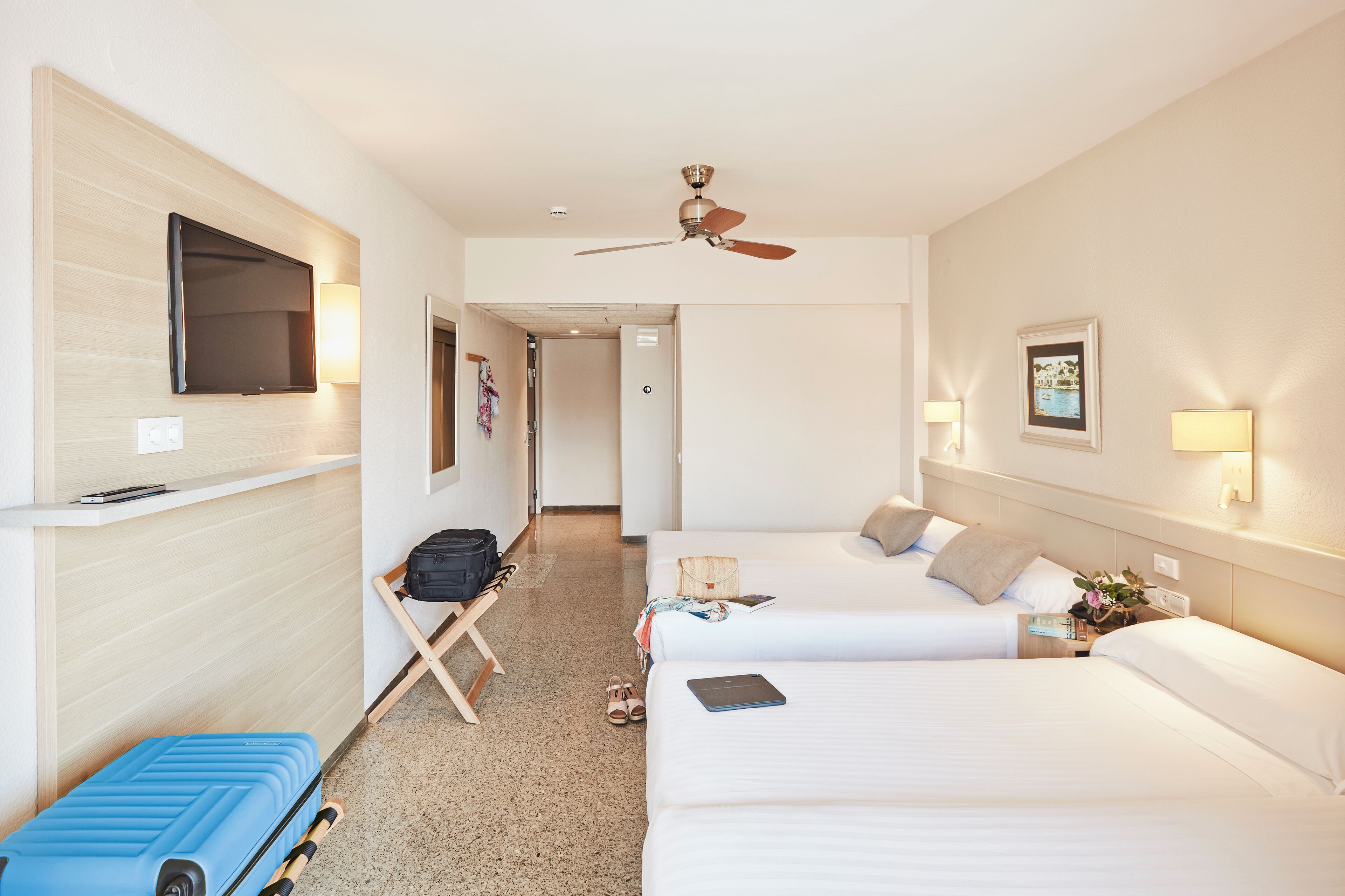 A hotel room with two beds, a ceiling fan, a flat-screen TV mounted on the wall, and a desk with a laptop.