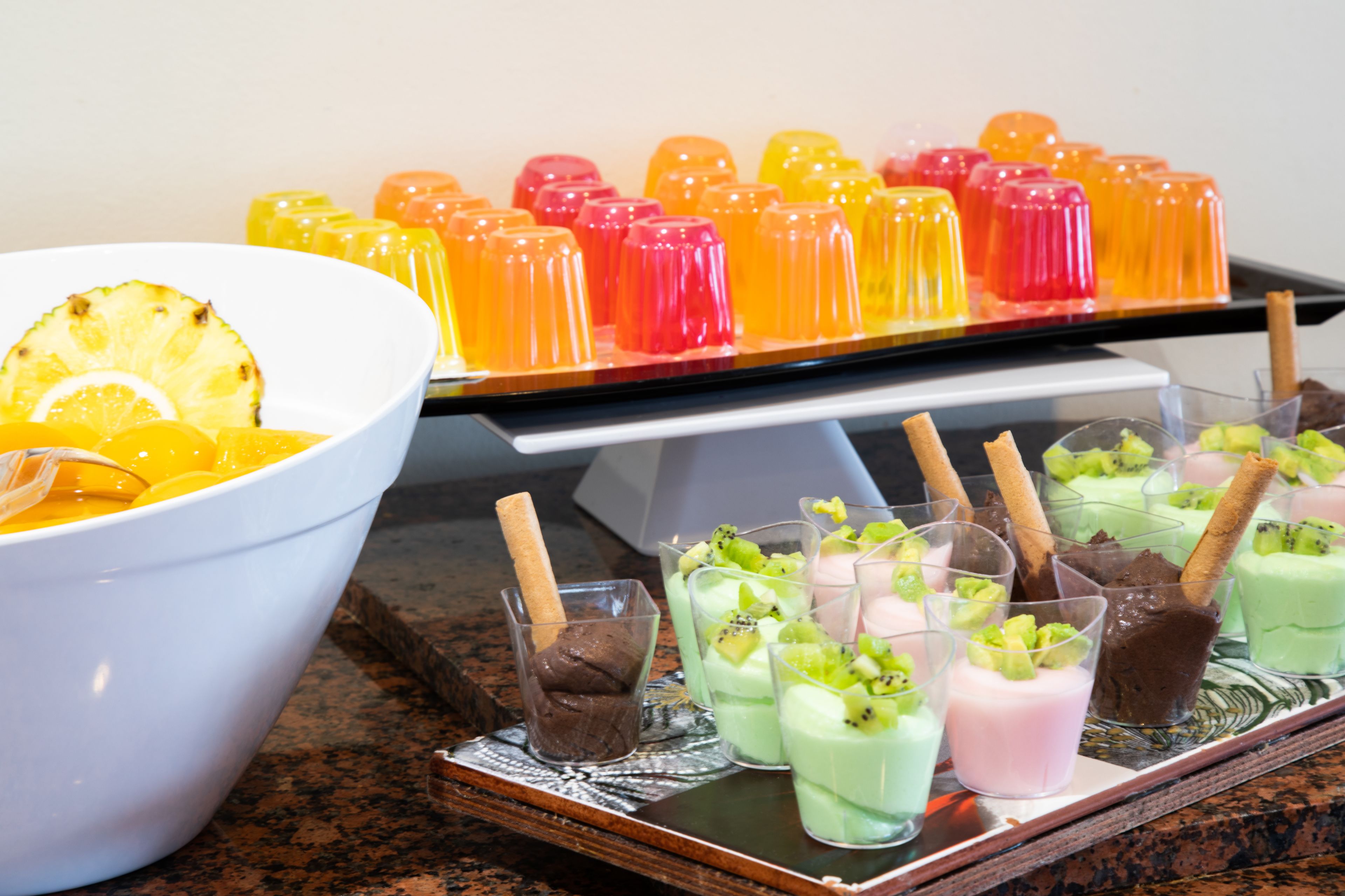 A dessert display with various colorful jellies and a bowl of fruit.
