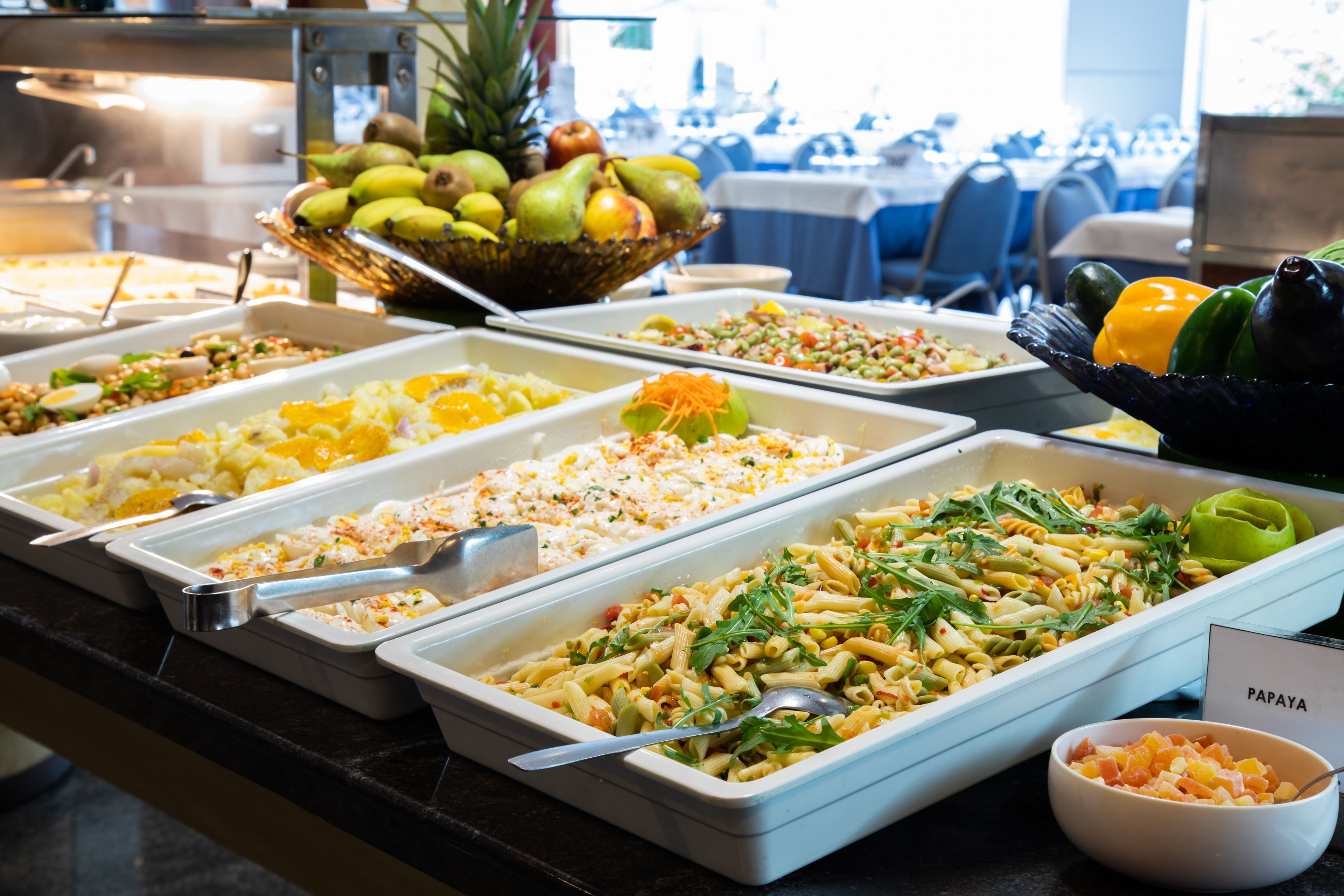 Un buffet proposant divers plats, notamment une salade de pâtes, des fruits et des légumes.