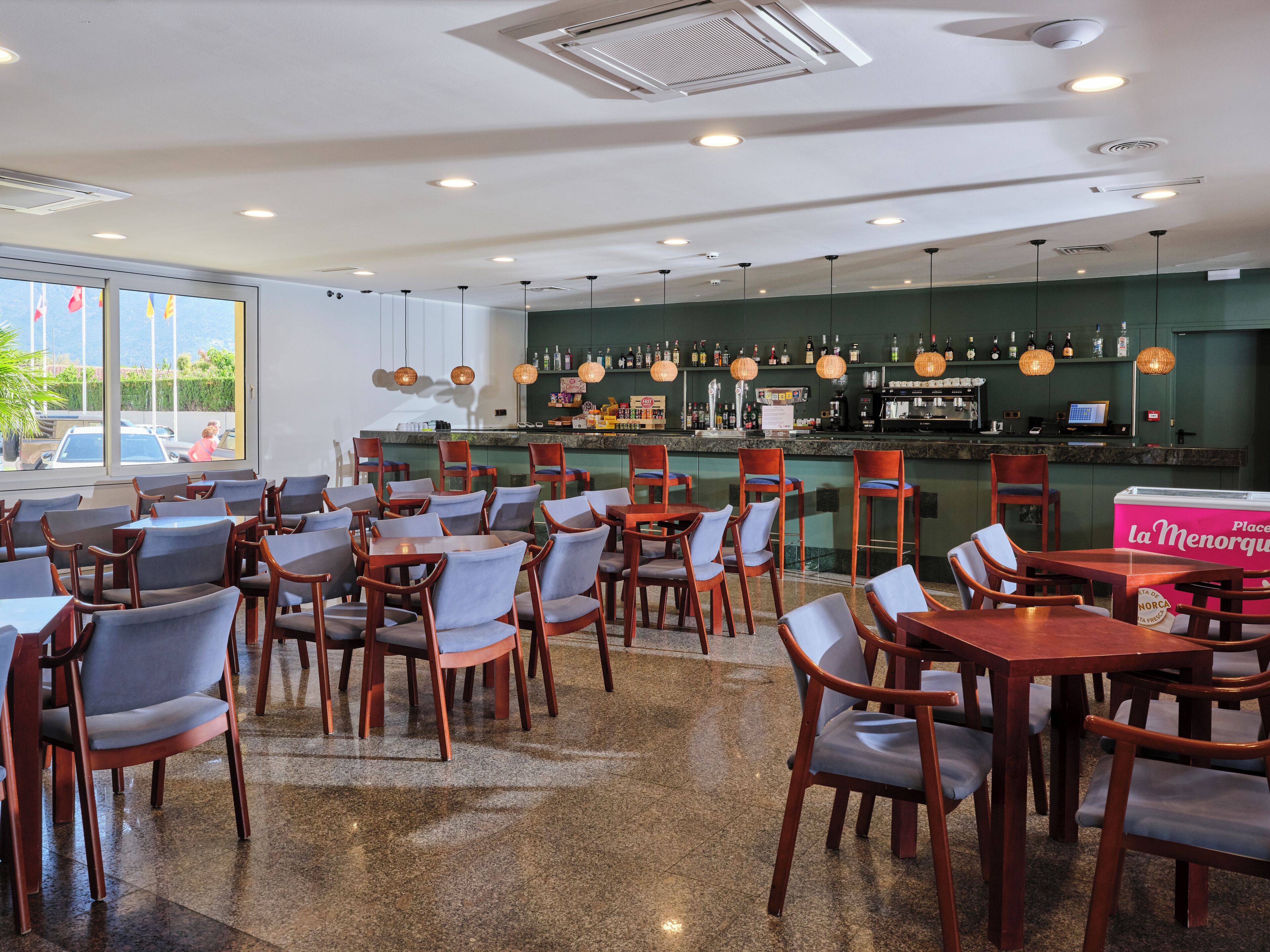 A restaurant with a bar area, seating arrangements, and a view of the outside.