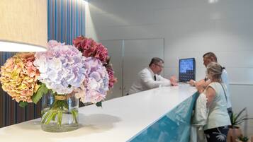 Un mostrador de recepción con un jarrón de flores, una pantalla digital y una barra.