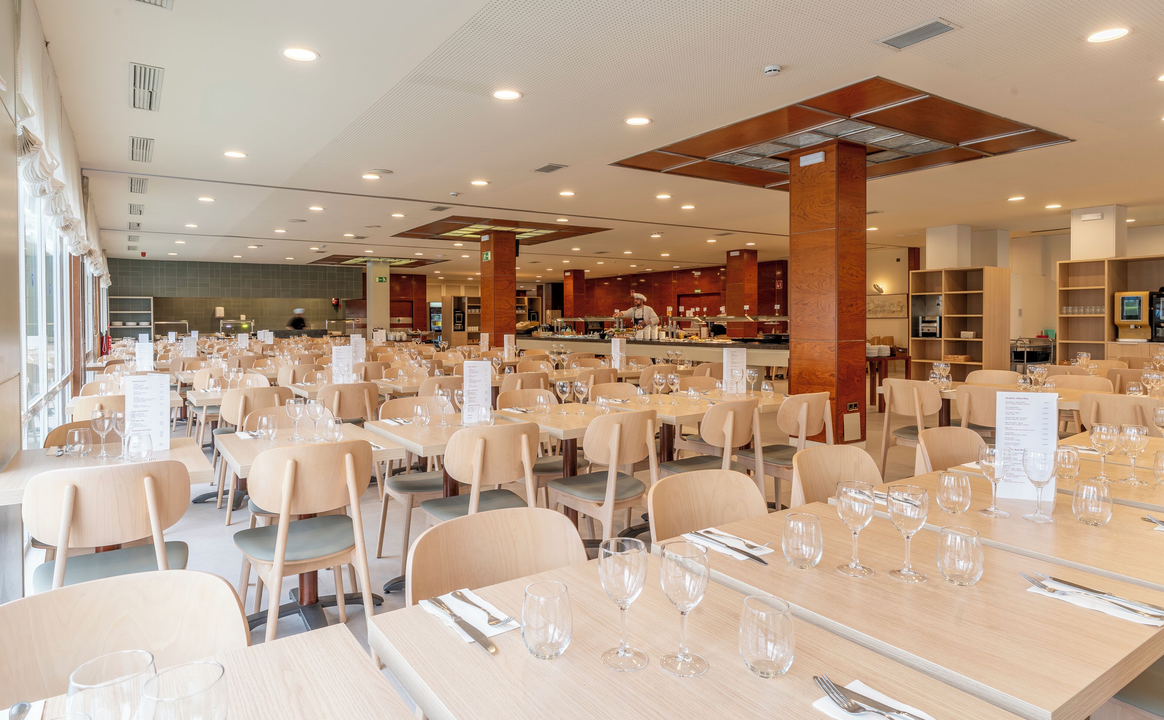 A spacious restaurant with multiple tables and chairs, a kitchen area in the background, and a clean, modern interior design.