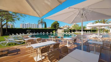 Zona de piscina amb gandules, taules i ombrel·les.