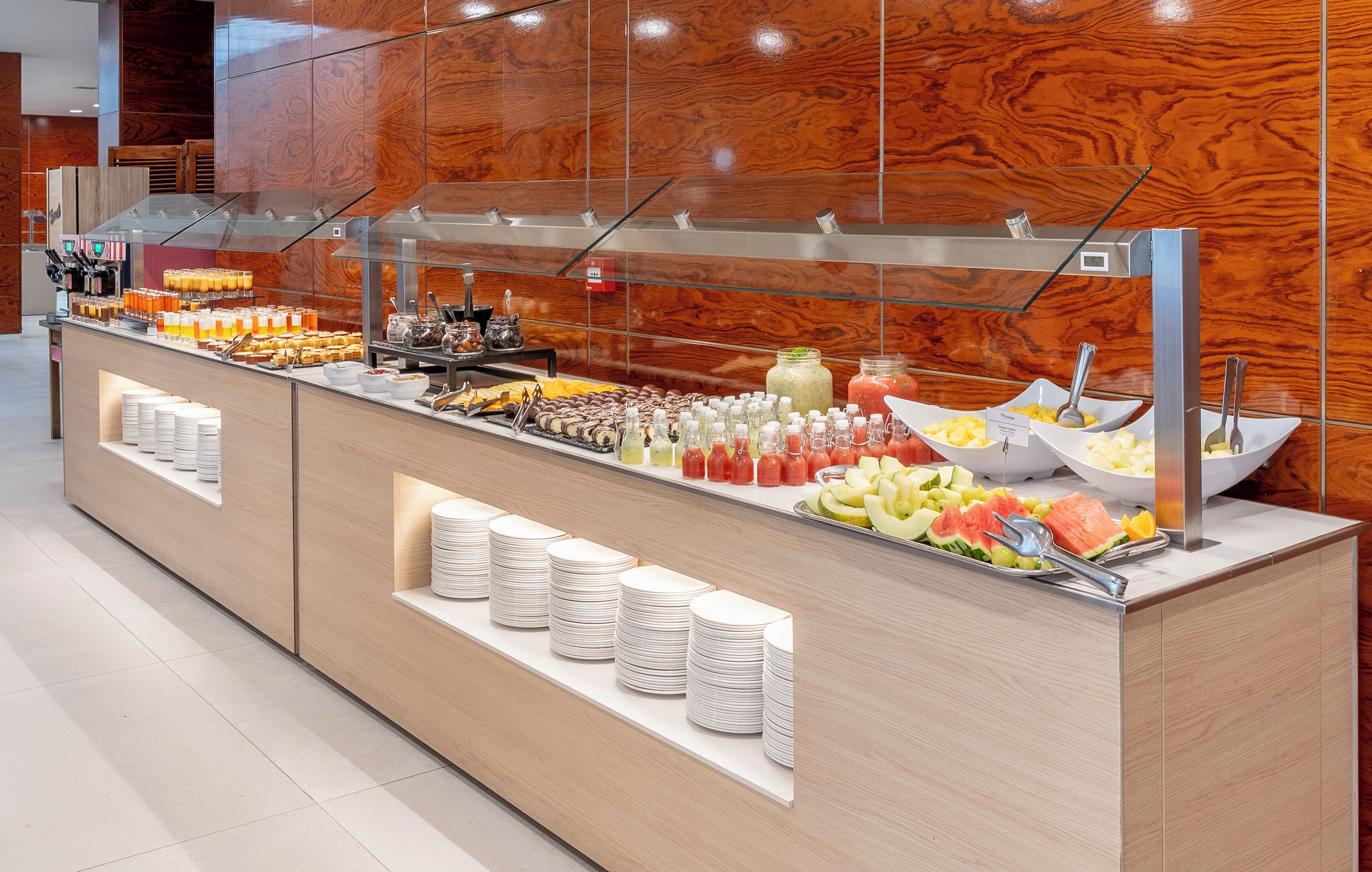 A buffet with various food items and condiments, including fruits, vegetables, and beverages.