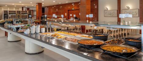 Ein reichhaltiges Buffet mit verschiedenen Speisen und eine Sitzgelegenheit mit Tischen und Stühlen.
