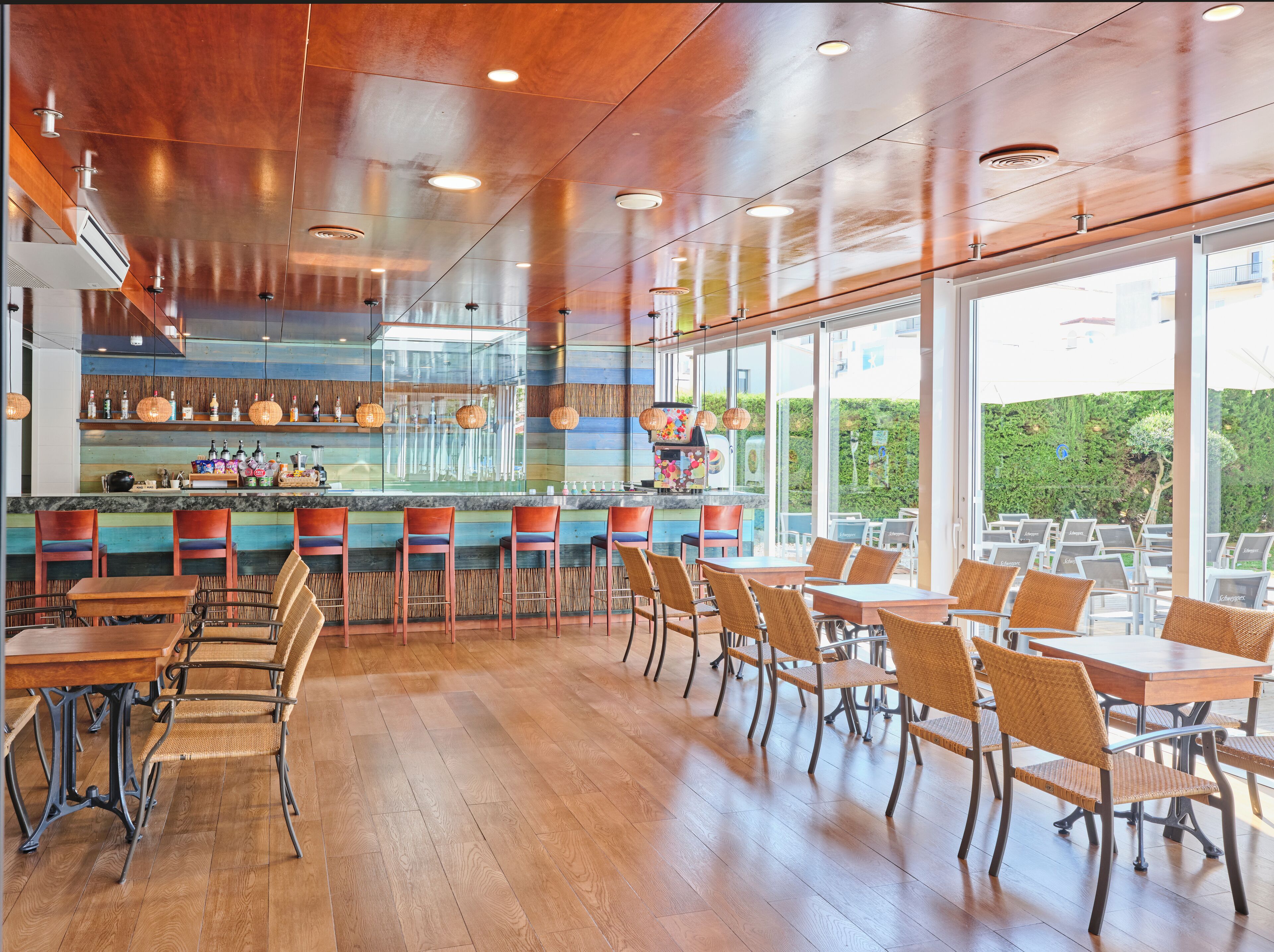 A restaurant with wooden floors, a bar area, and outdoor seating with a view of greenery.