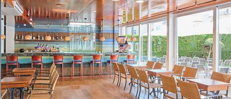 A restaurant with wooden floors, a bar area, and outdoor seating with a view of greenery.