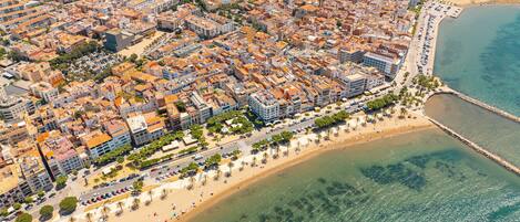An aerial view of a coastal city with dense urban buildings, a beach, and a pier.