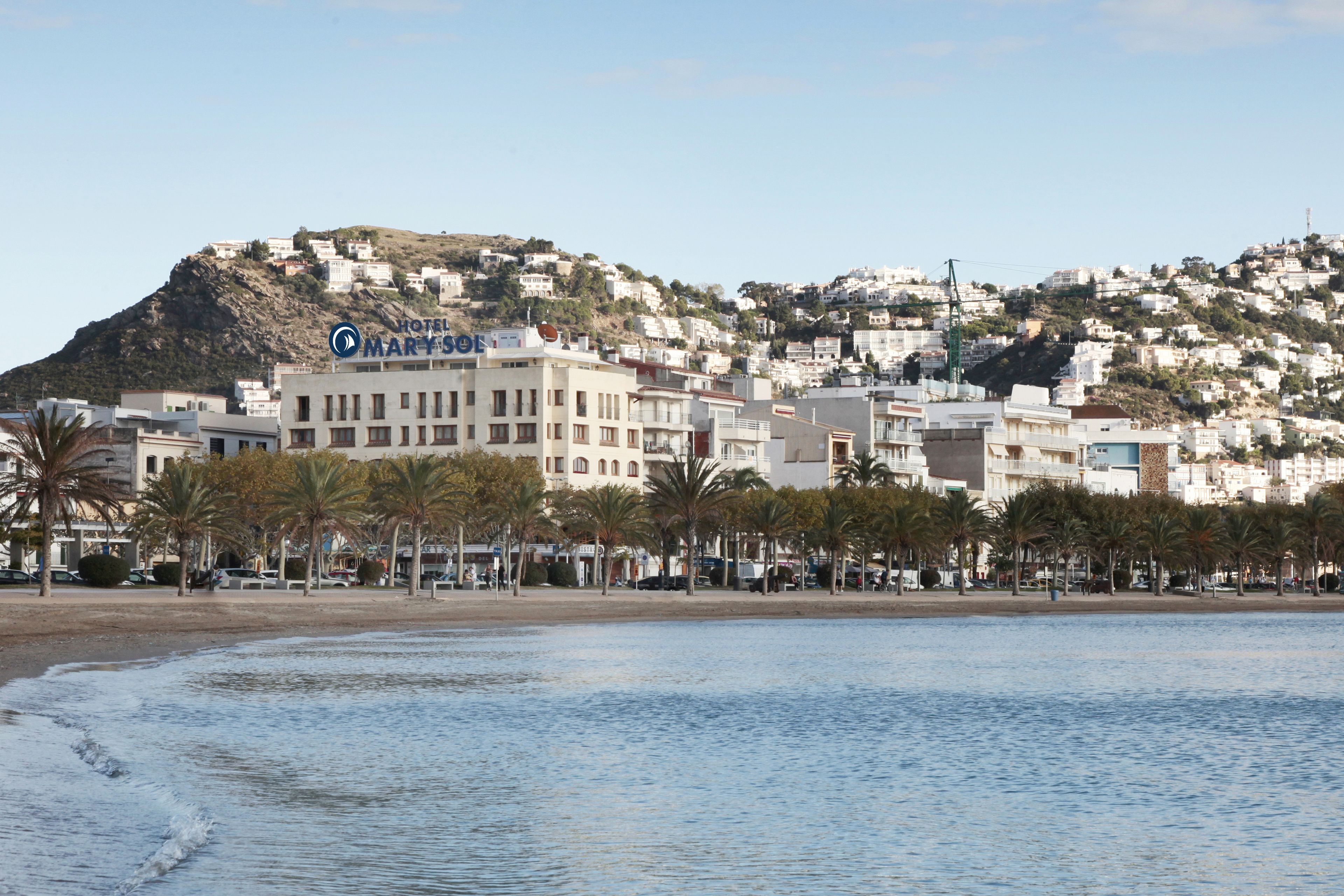 A coastal hotel with a view of the sea and a hillside in the background.